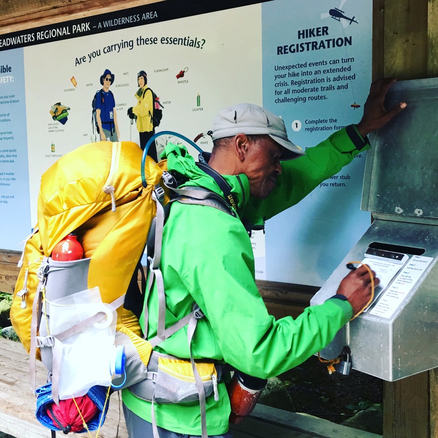 Man stands in front of an information board at the beginning of a hike. He is filling out a registration form with his trip plan.