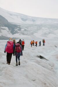A group of people with large backpacks in single file doing an ice walk